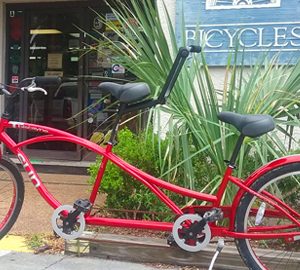 pedals red tandem bike in front of store